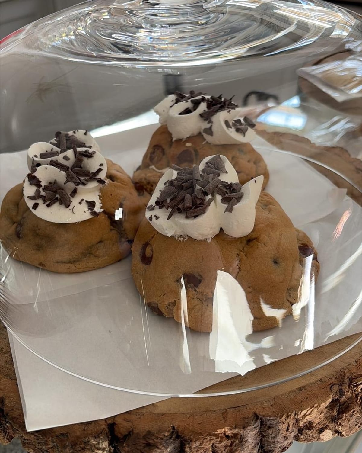 Chocolate chip cookies topped with cream and chocolate shavings under a glass cloche