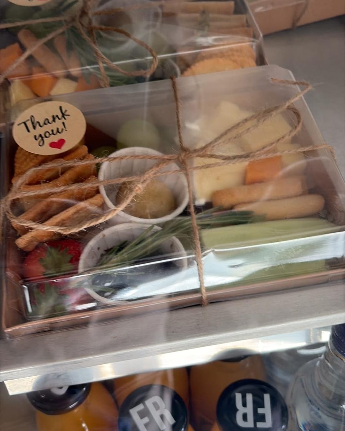 Clear graze boxes tied with twine, holding crackers, cheese, fruit and dips, each with a thank-you sticker