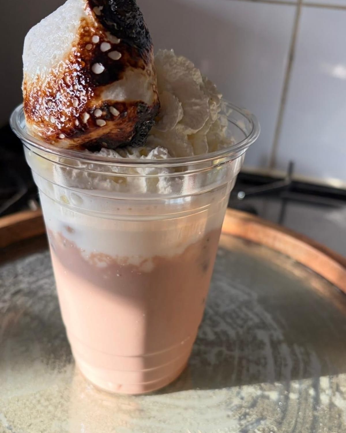 A pink strawberry milkshake in a clear cup, topped with cream and a toasted marshmallow