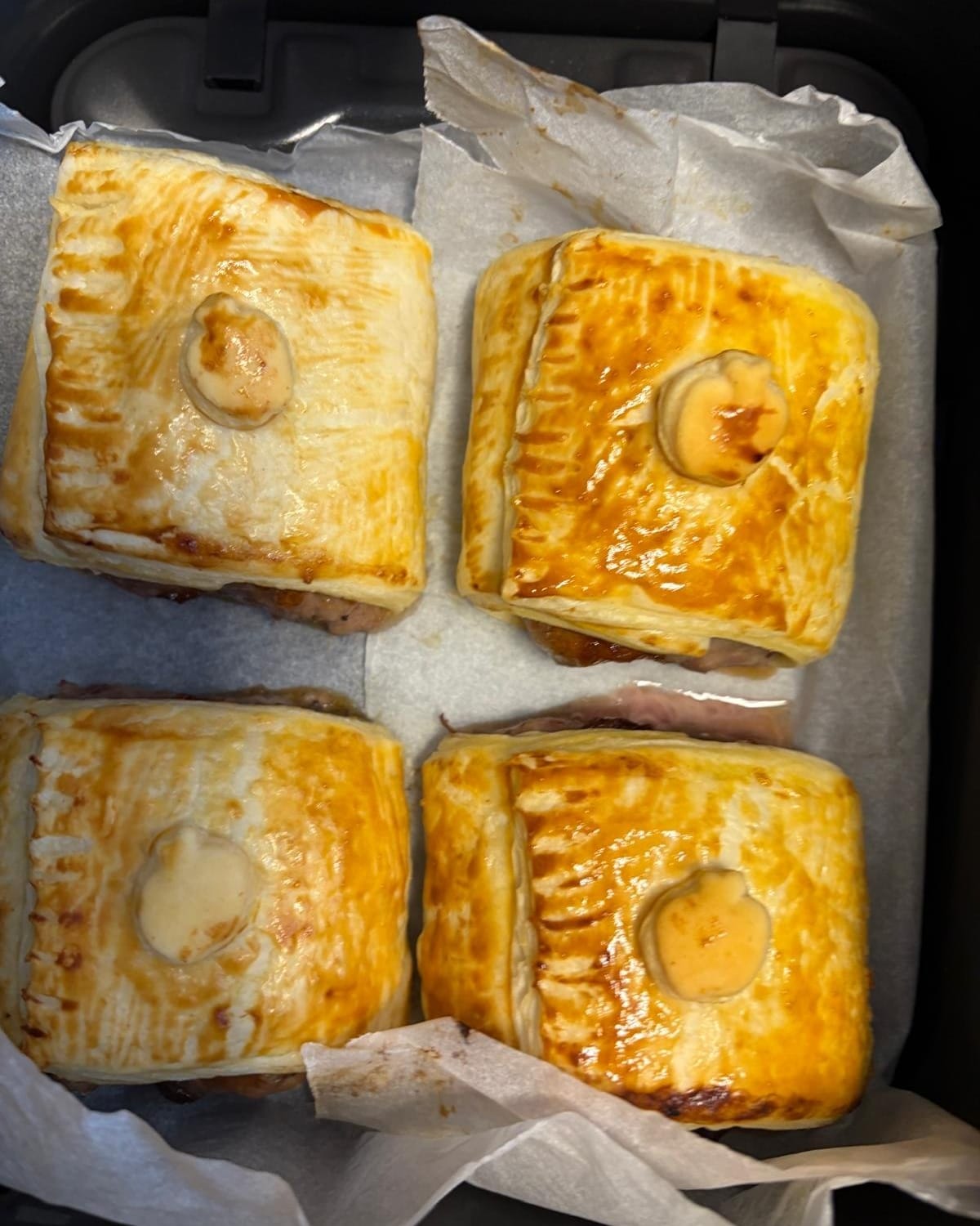 Four golden pasties on baking paper in an air fryer basket