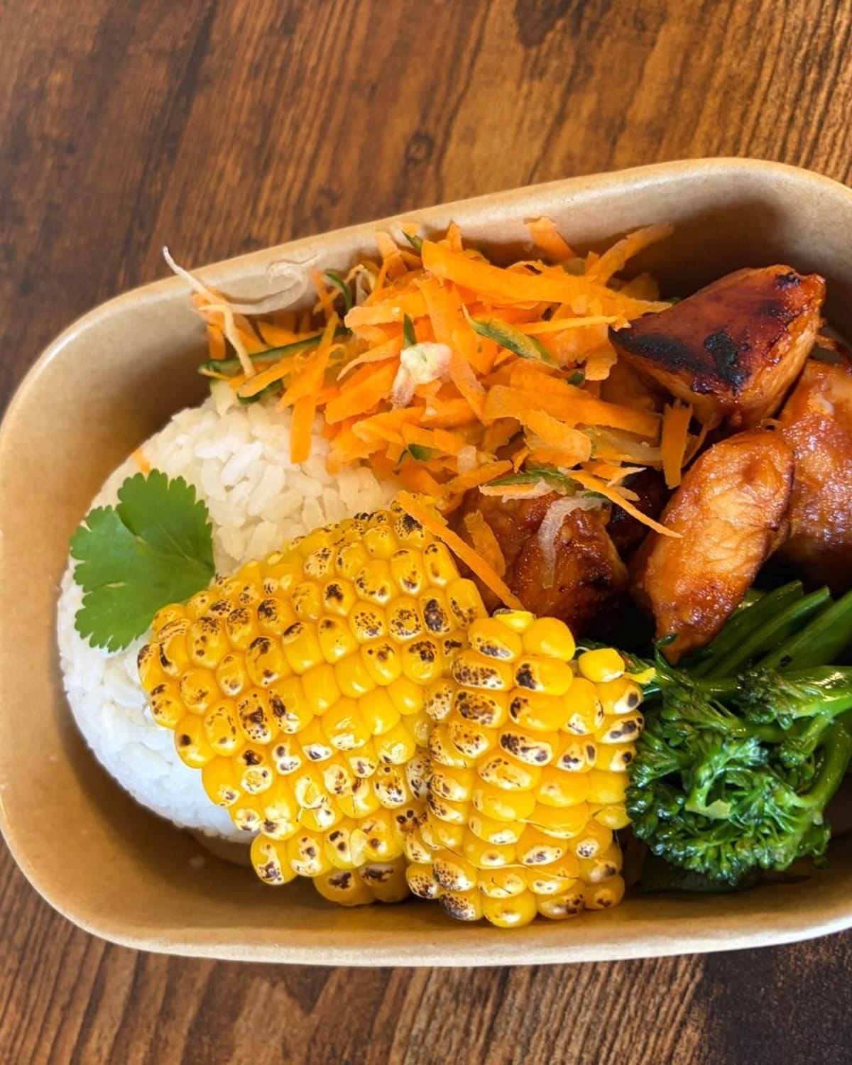 A rice bowl with glazed chicken, charred corn, pickled carrot and greens