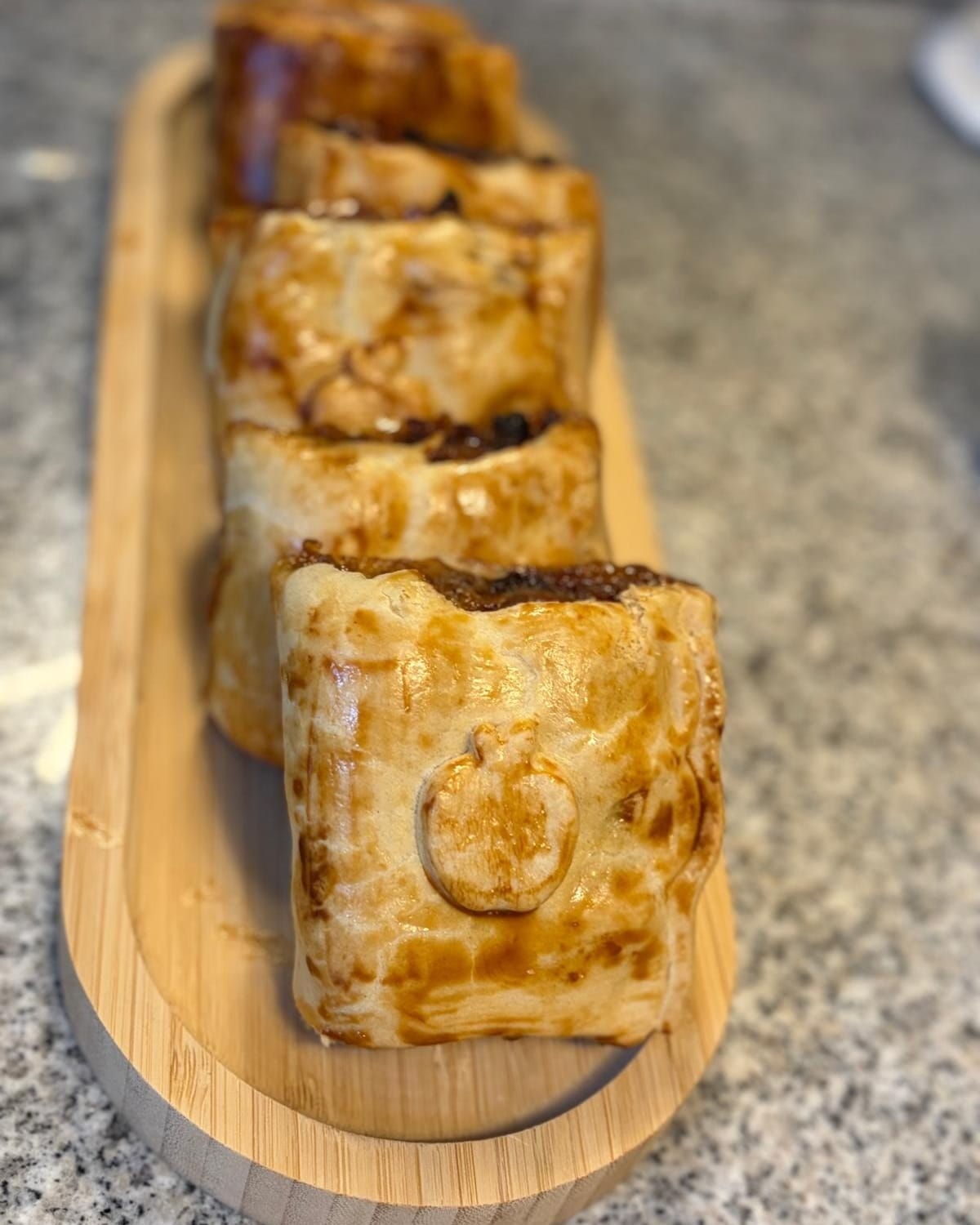 Sausage rolls in a row on a wooden board, glazed and browned