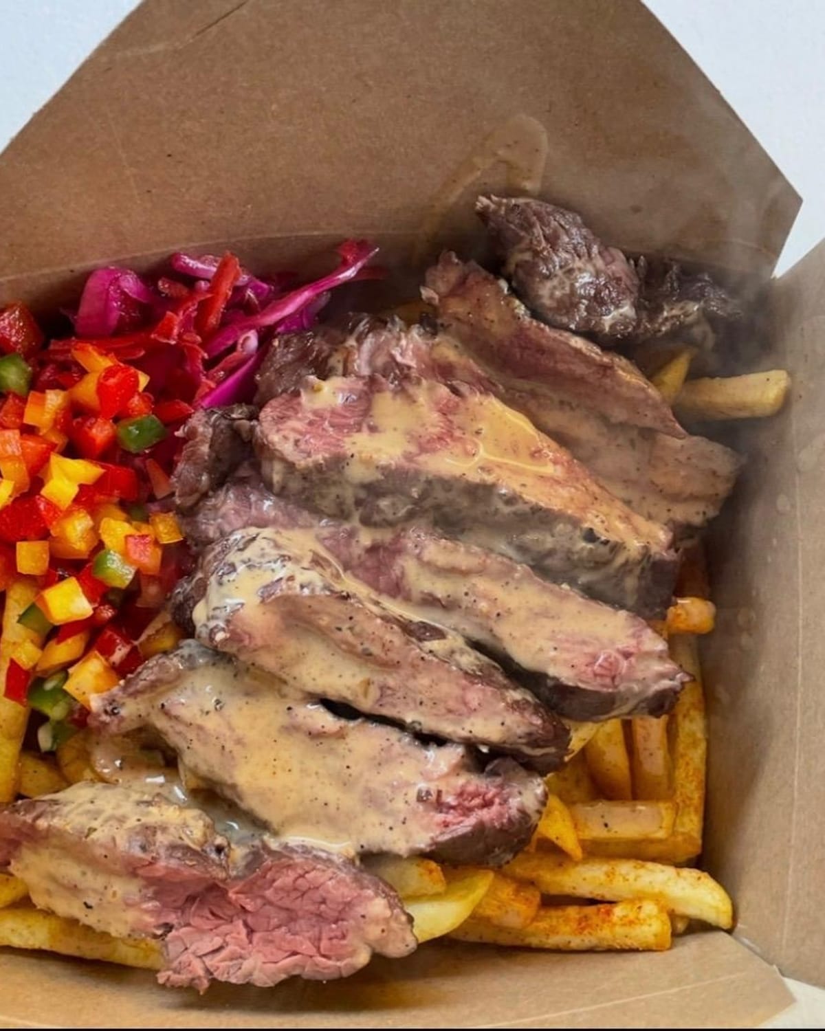 Sliced steak with peppercorn sauce over fries, with pickled cabbage and peppers, in a Kraft box