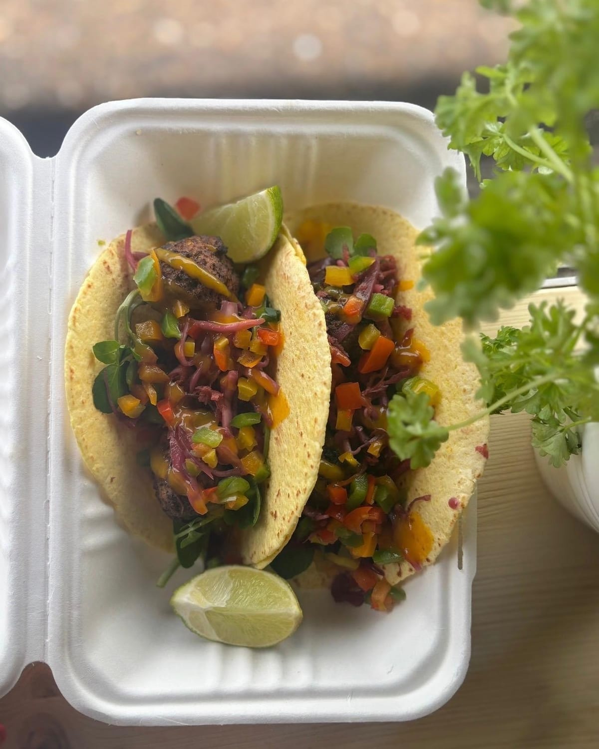 Two soft tacos filled with spiced vegetables, red cabbage and lime in an open takeaway box