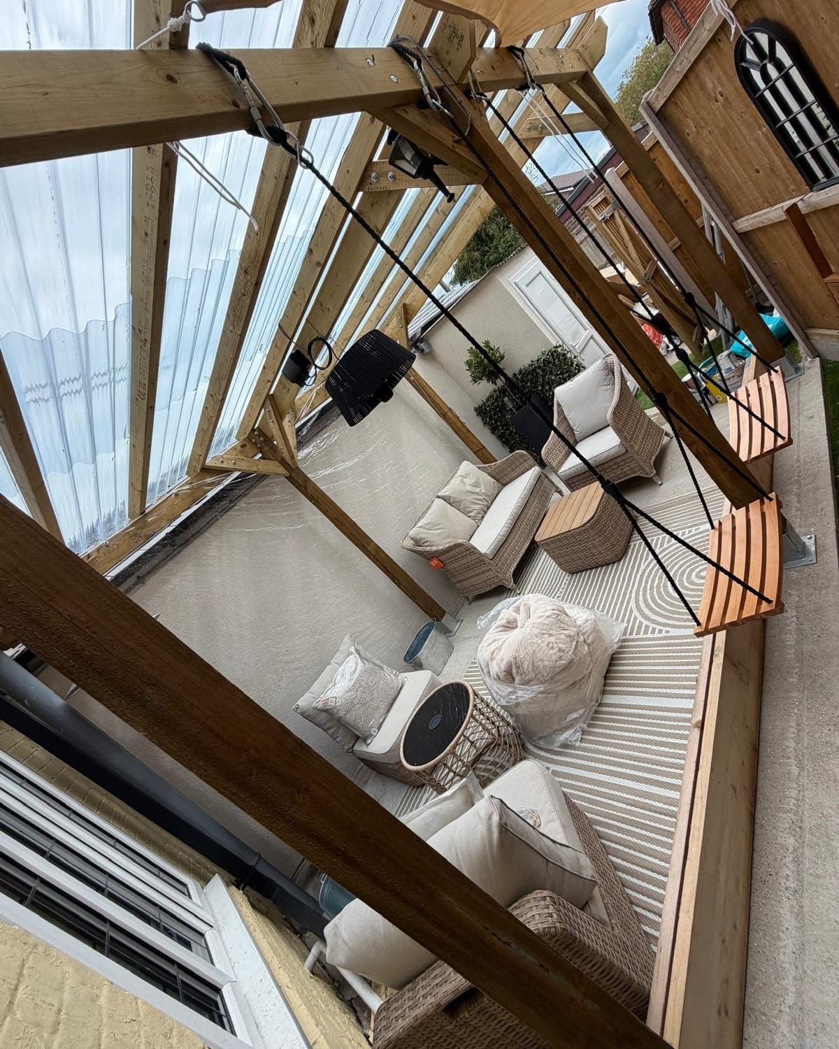 The covered garden seating: rattan armchairs, a striped rug and hanging wooden swing seats under a timber pergola