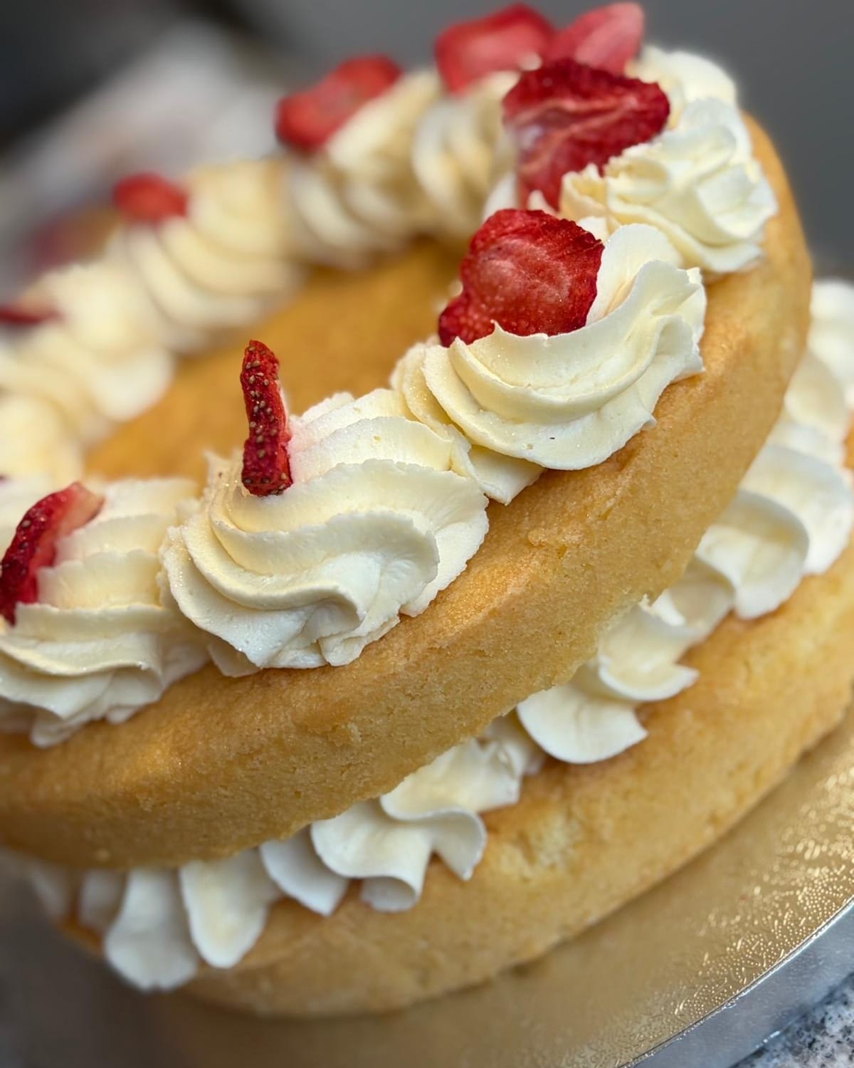 A Victoria sponge filled and topped with cream and strawberry pieces, on a cake stand in the display fridge